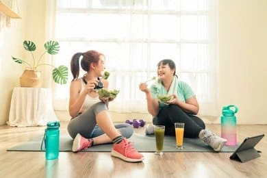 Two women enjoying healthy salads and smoothies after a workout.